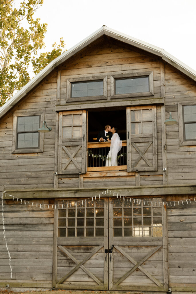 wedding couple kissing through barn doors of a wedding venue in kansas city